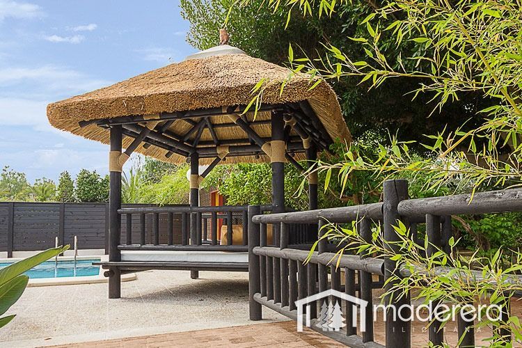 Un cenador con techo de paja se encuentra junto a una piscina.