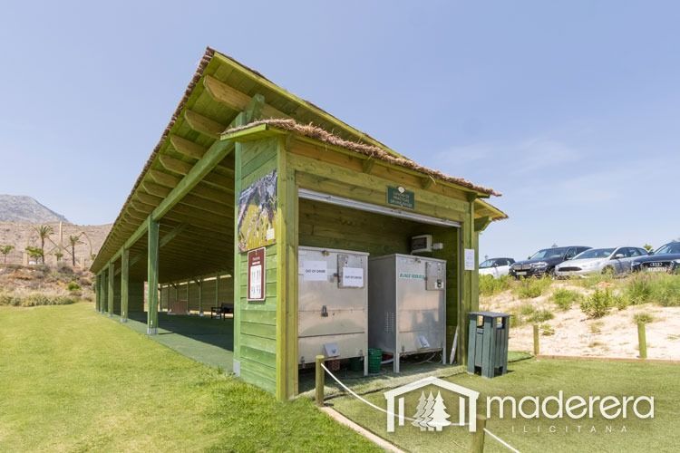 Un edificio de madera con techo verde se encuentra encima de un exuberante campo verde.