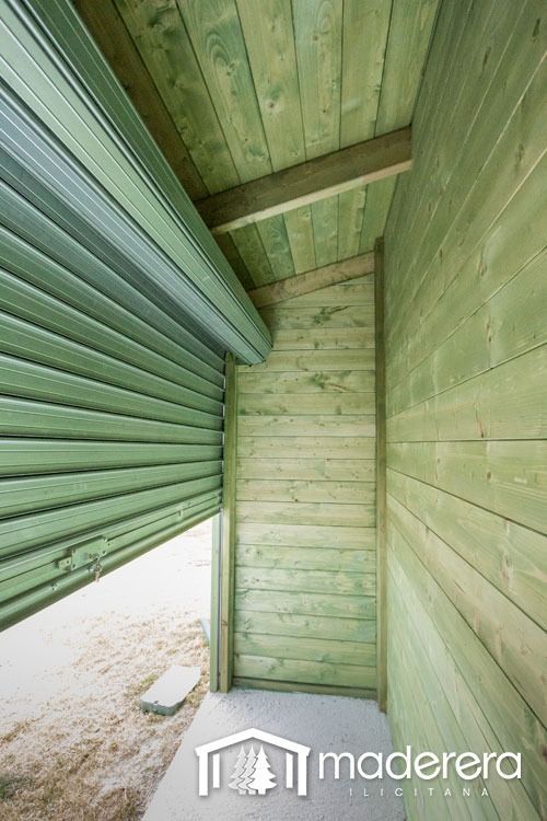 Un edificio de madera verde con una puerta enrollable abierta.