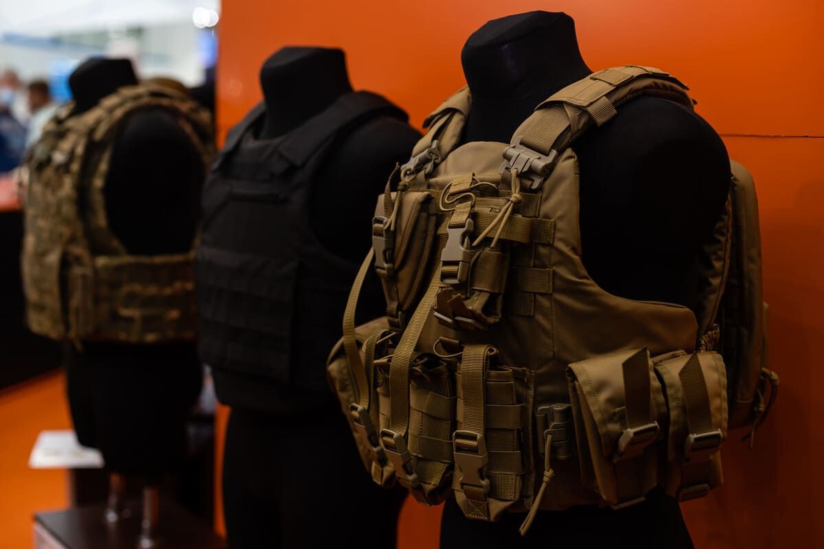 Dos maniquíes con chalecos tácticos se exhiben frente a una pared naranja.