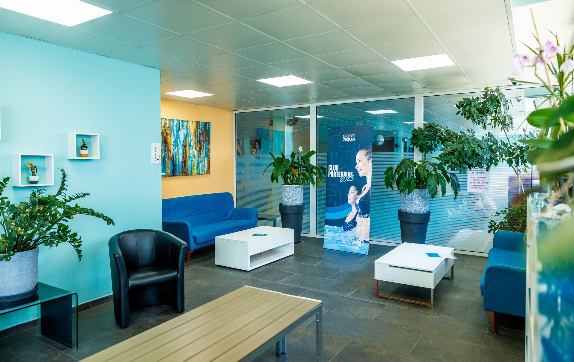 Espace d'accueil avec un bureau bleu, une enseigne blanche, un distributeur automatique et des plantes d'intérieur.