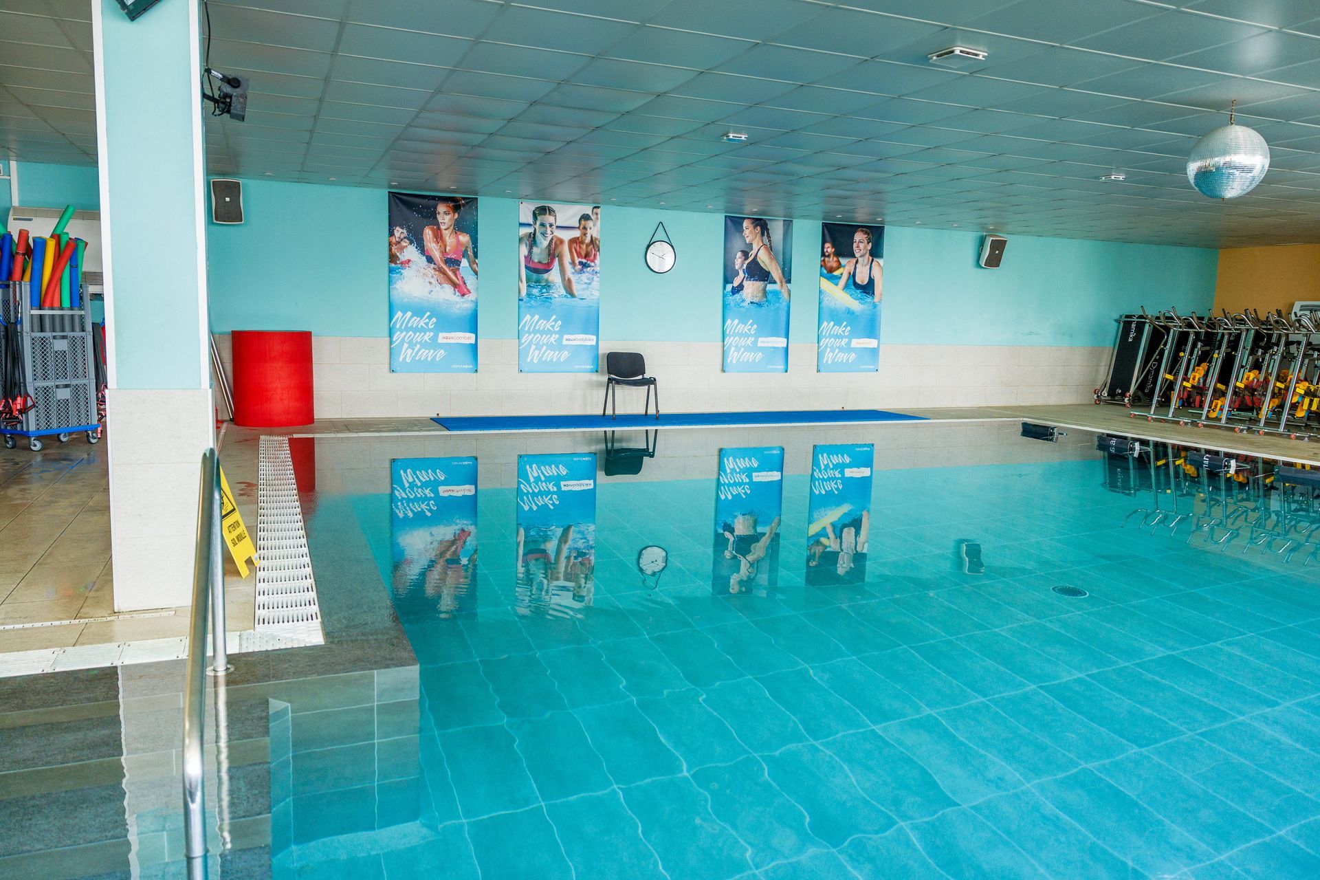 Piscine intérieure à l'eau bleu clair, murs carrelés, affiches publicitaires et une rangée de vélos.