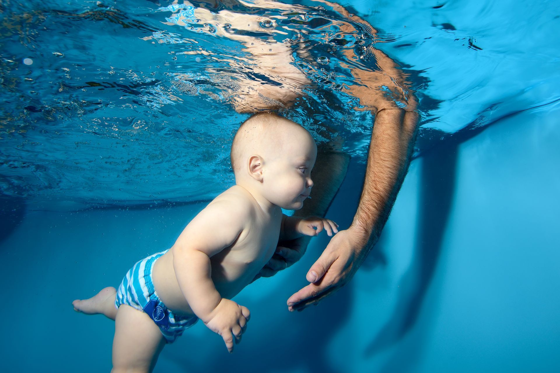 Une femme en maillot tient à l'horizontale un bébé portant une couche de bain rose.