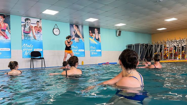 Un moniteur de fitness anime un cours d'aquagym dans une piscine, avec des participants dans l'eau.