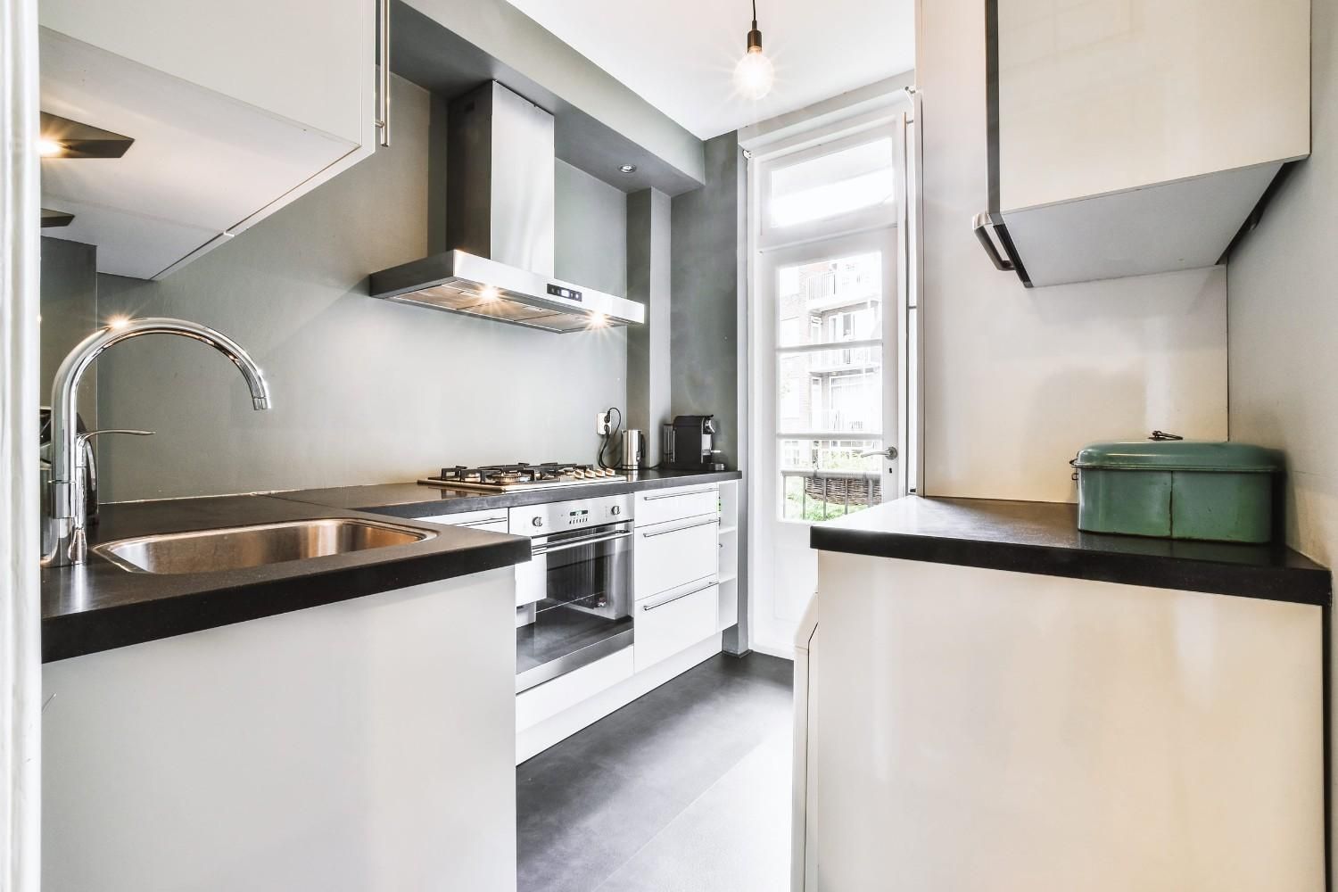 Una cocina moderna tipo galera con gabinetes blancos, encimeras oscuras, campana extractora de acero inoxidable.