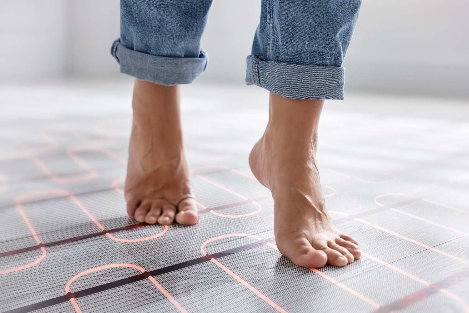 Pies descalzos caminando sobre un suelo con cables de calefacción radiante de color naranja visibles.