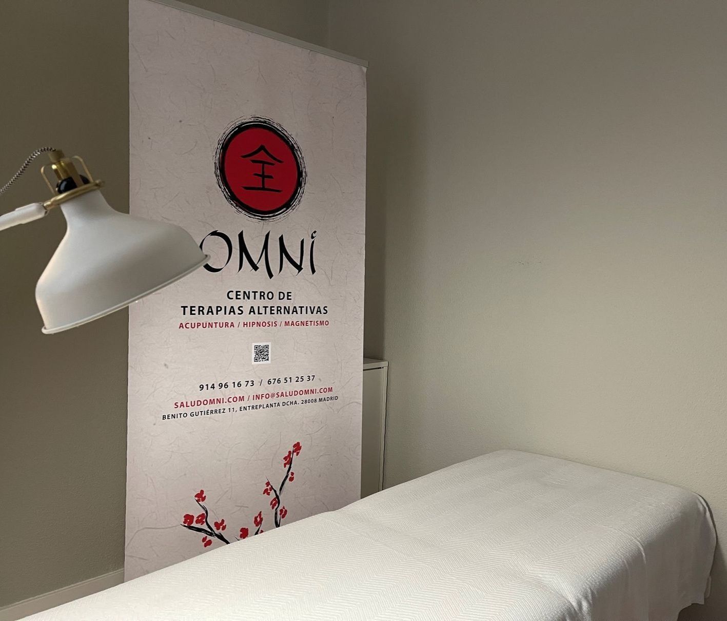 Sala de tratamiento con camilla de masaje, lámpara y cartel para un centro de terapia.