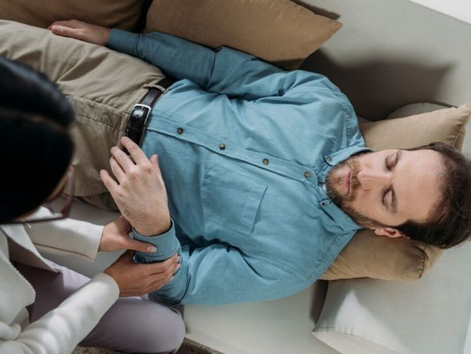 Persona tumbada en un sofá, con el brazo sujetado por otra persona, en el interior.