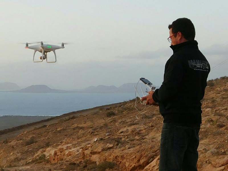 Un hombre sostiene un control remoto mientras un dron vuela por encima.