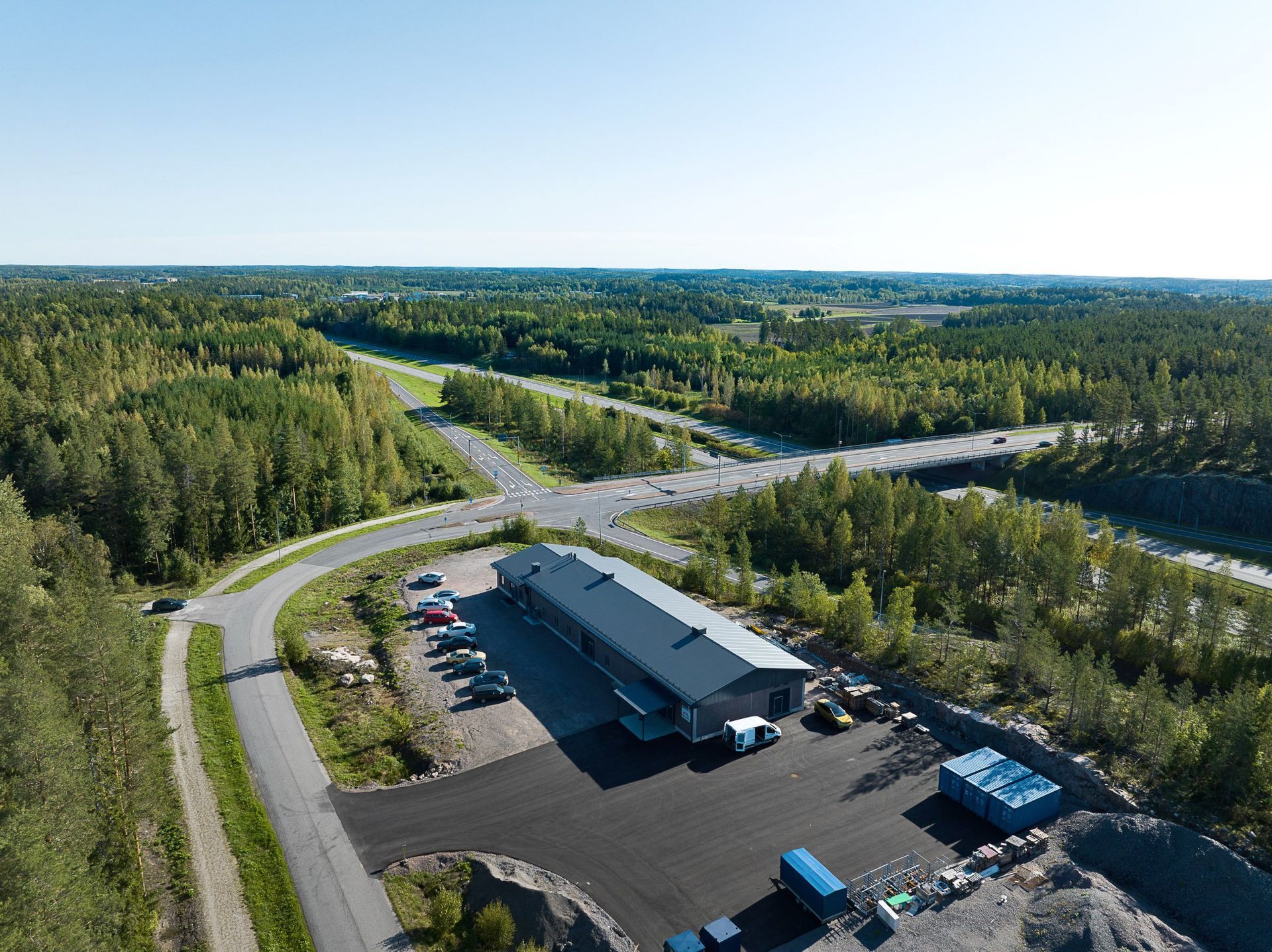 Ilmakuva metsäisestä teollisuusalueesta, jossa on pitkä varasto, pysäköityjä kuorma-autoja ja lähellä olevia teitä