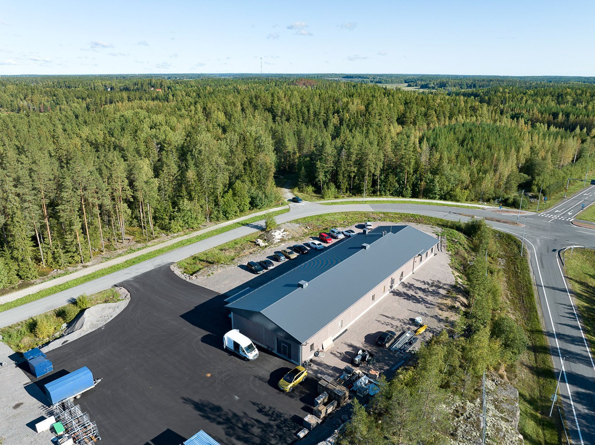 Ilmakuva metsän vieressä olevasta varastosta, jossa on pysäköityjä kuorma-autoja ja päällystetty tontti teiden risteyksessä