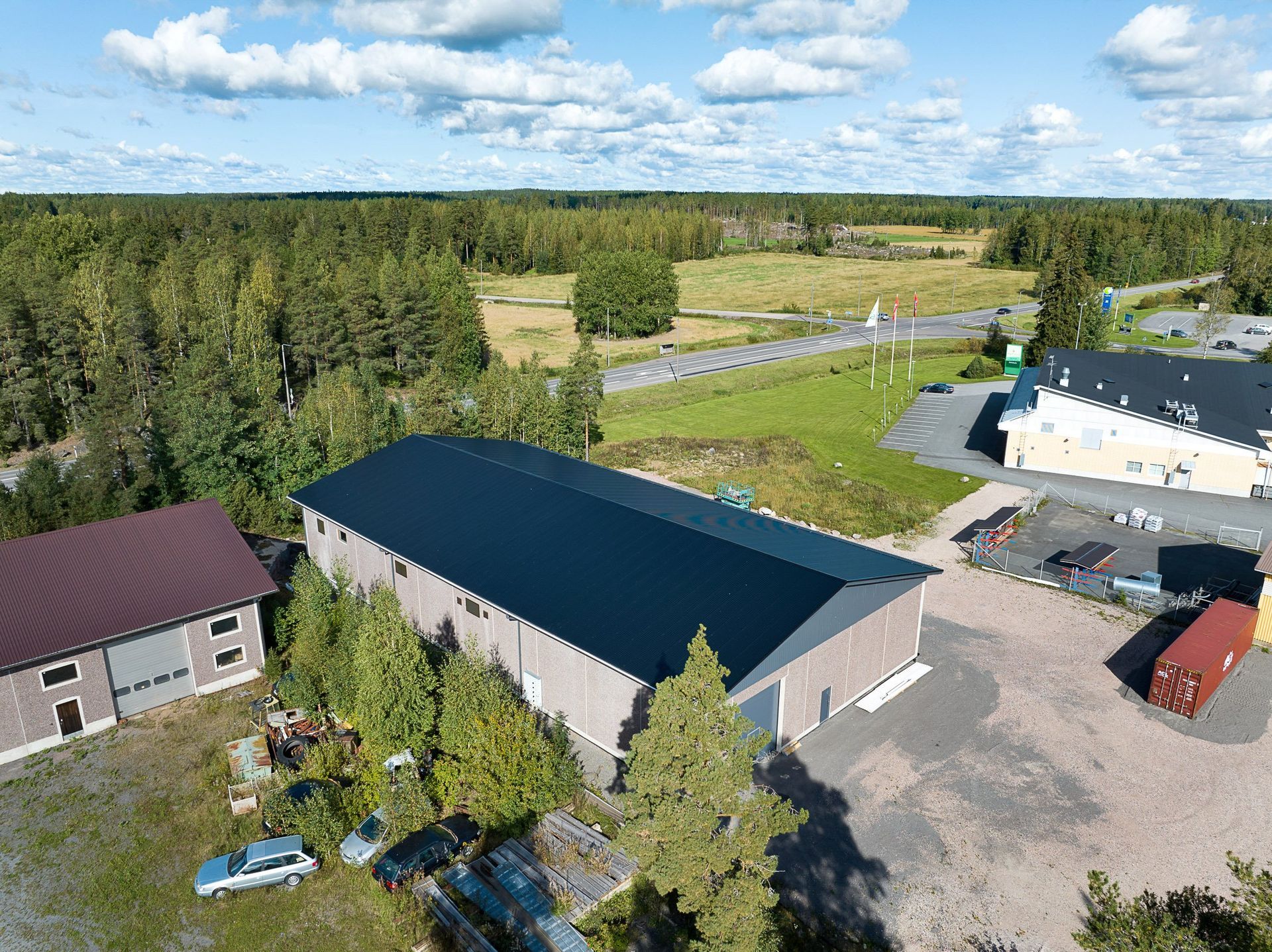 Ilmakuva maatilan rakennuksista metsän vieressä ja pelloista sinisen taivaan alla