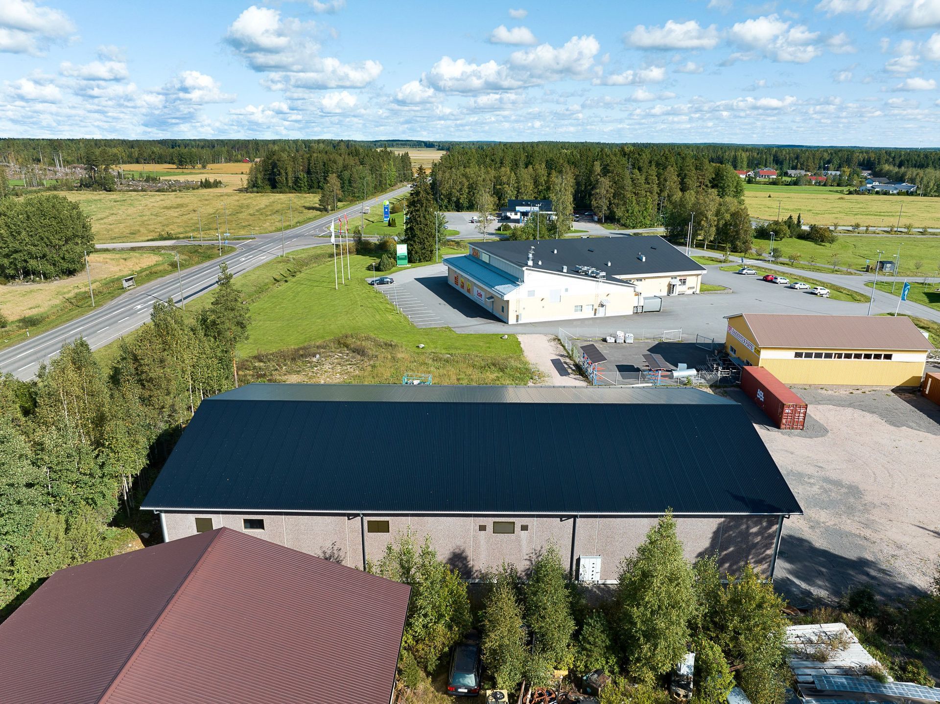 Ilmakuva maaseudun teollisuuspihasta, jossa on useita rakennuksia, pysäköintialueita ja peltojen vieressä oleva tie.