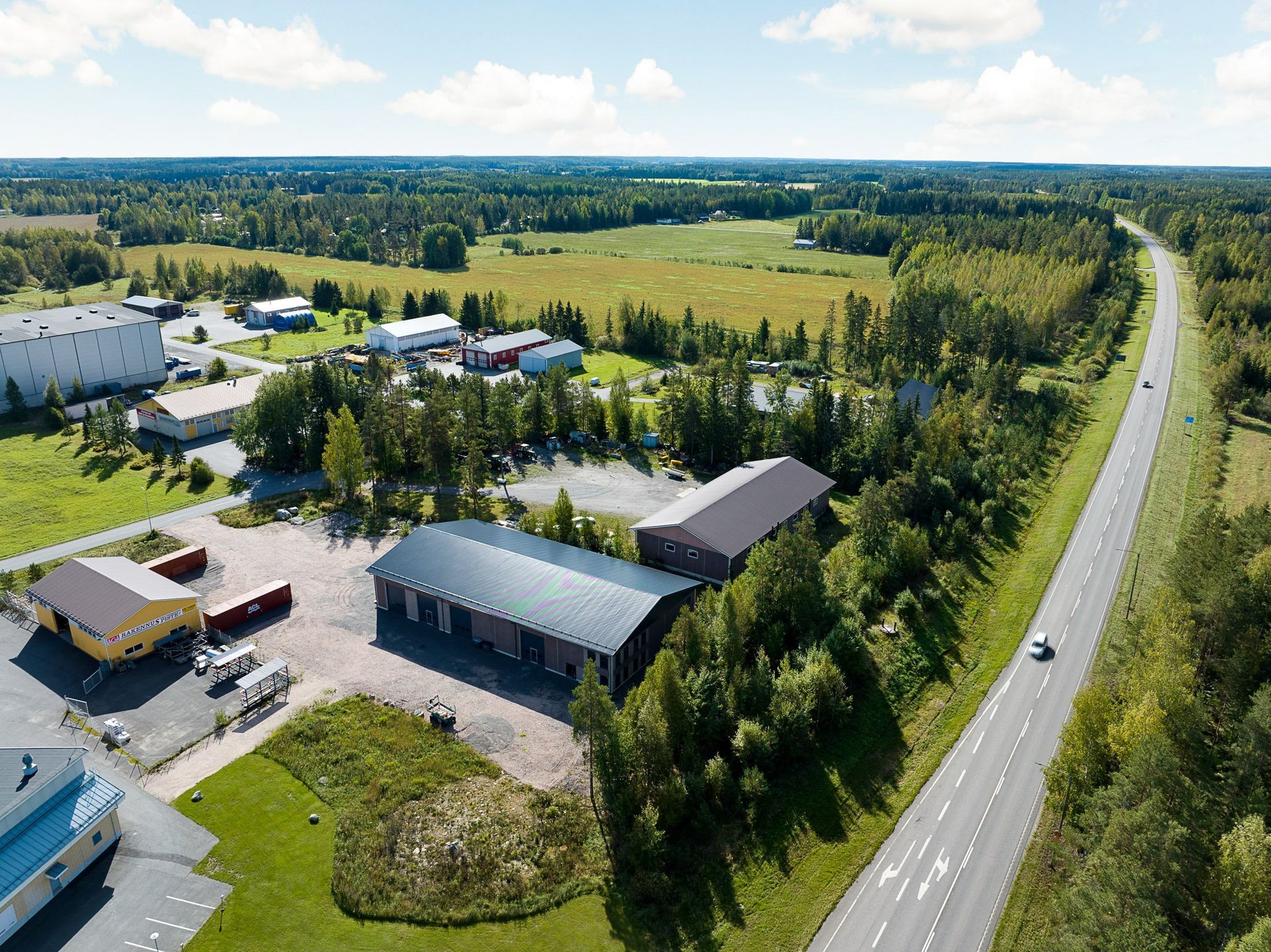 Ilmakuva maaseudun teollisuusalueesta moottoritien vieressä, puiden ja avoimien peltojen ympäröimänä.