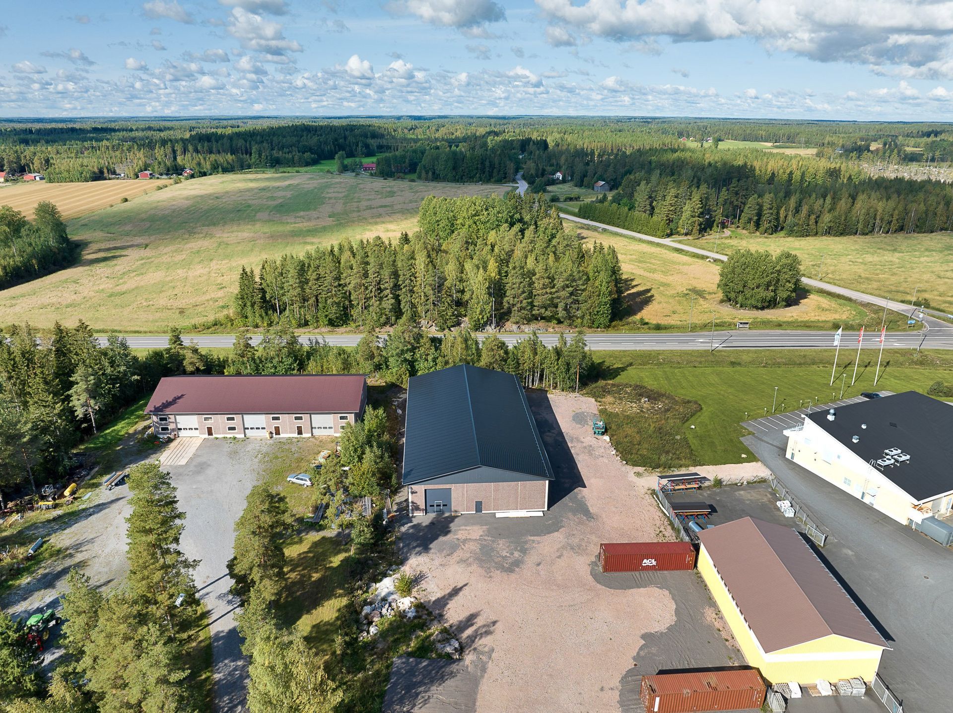 Ilmakuva maaseudun rakennuksista peltojen ja puiden vieressä sinisen taivaan alla