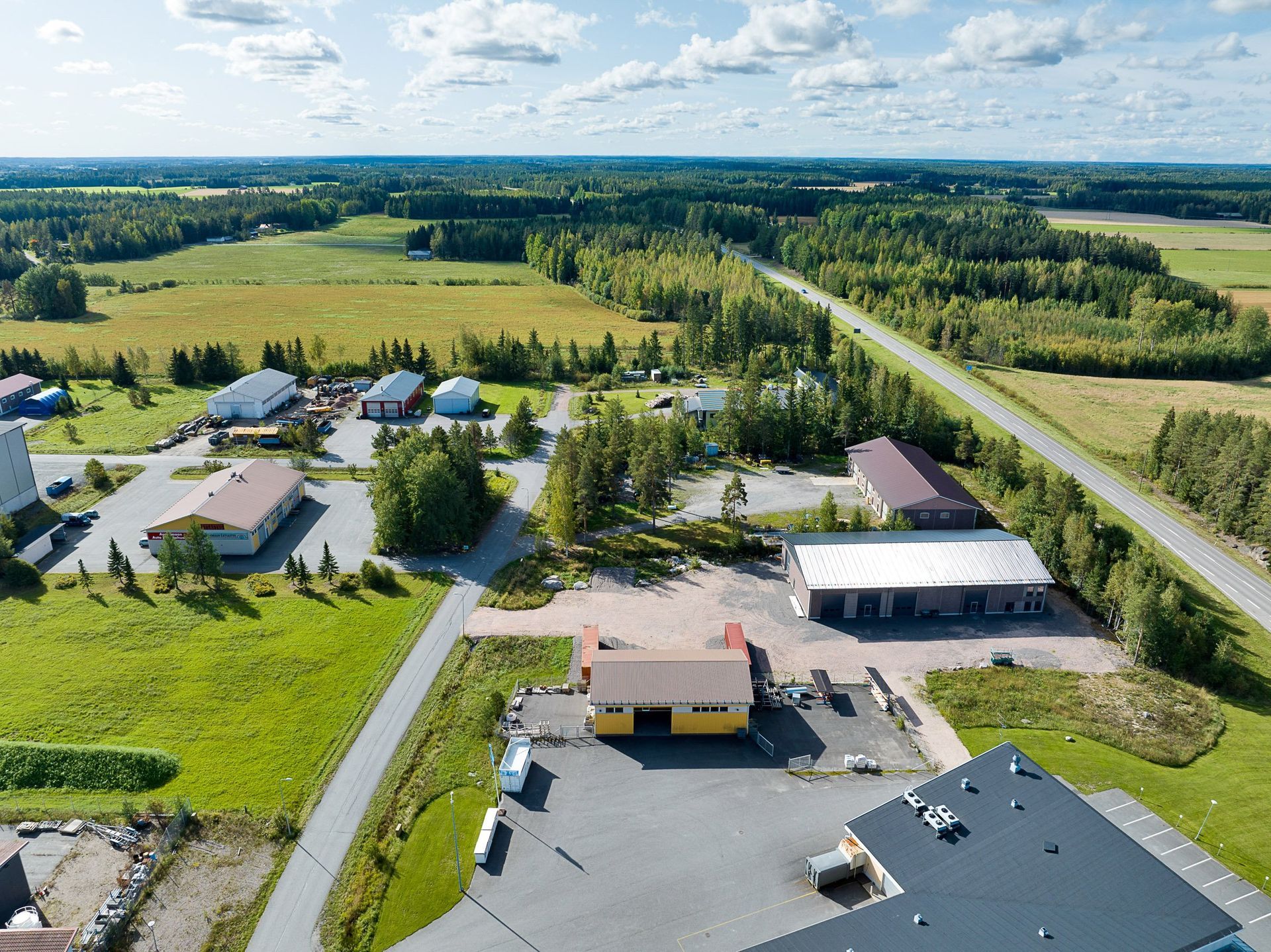 Ilmakuva maaseutunaapurustosta, jossa on koteja, peltoja ja pitkä tie pilvisen taivaan alla
