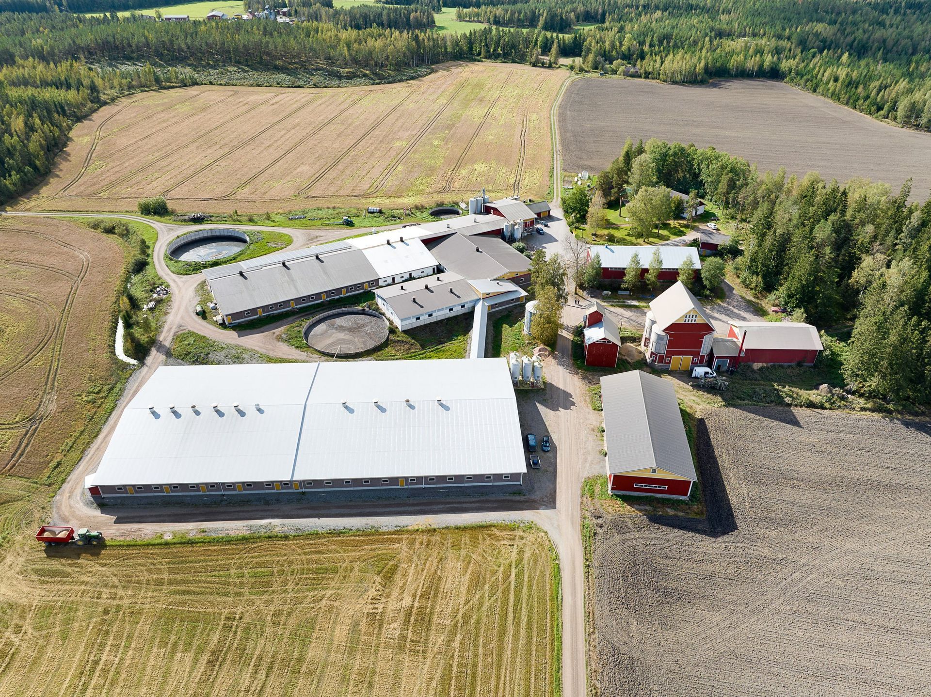 Ilmakuva maatilakompleksista, jossa on navettoja, siiloja, peltoja ja ympäröiviä puita