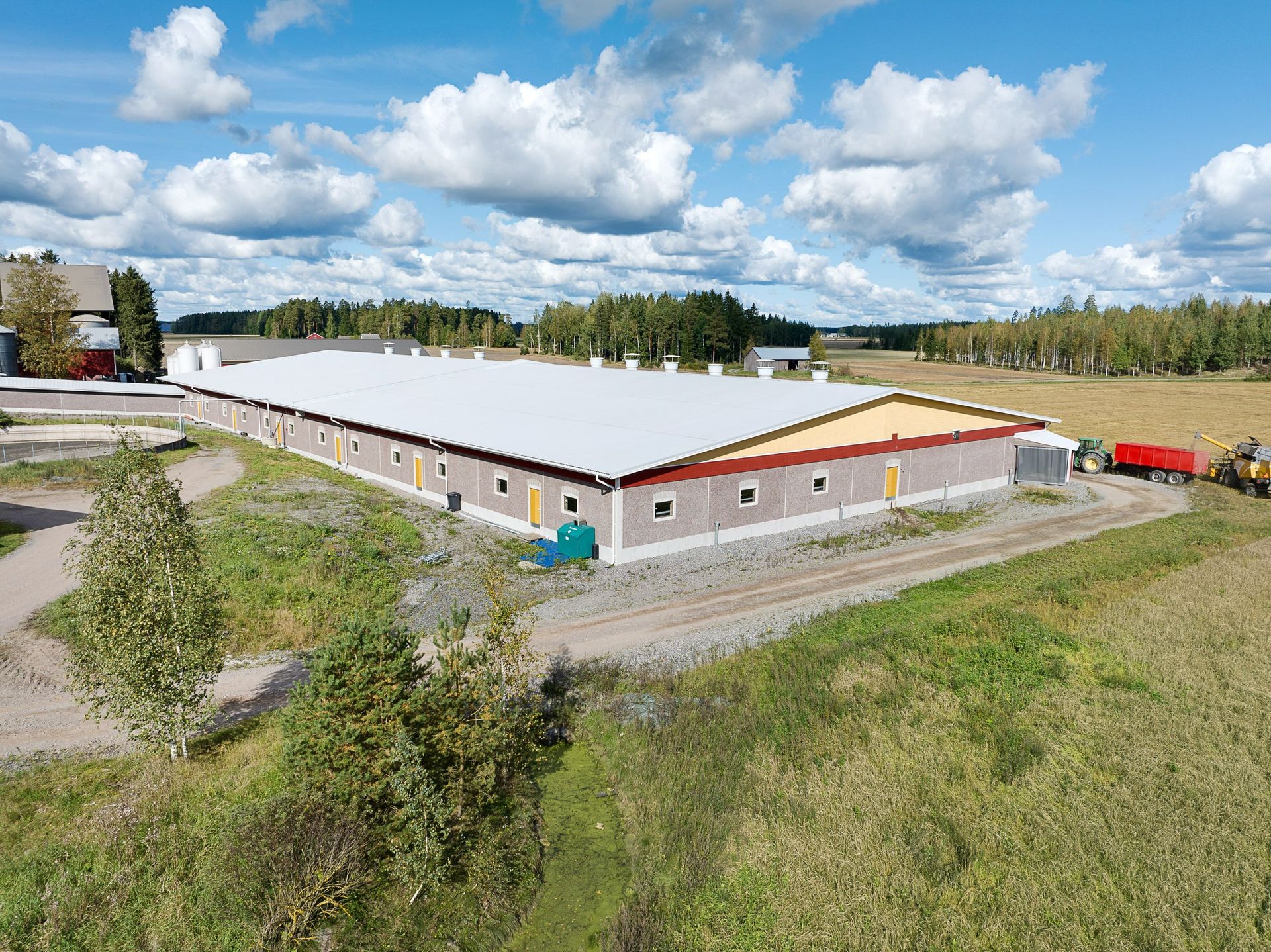 Ilmakuva suuresta valkoisesta varastosta, jossa on punainen katto, pilvisen sinisen taivaan alla