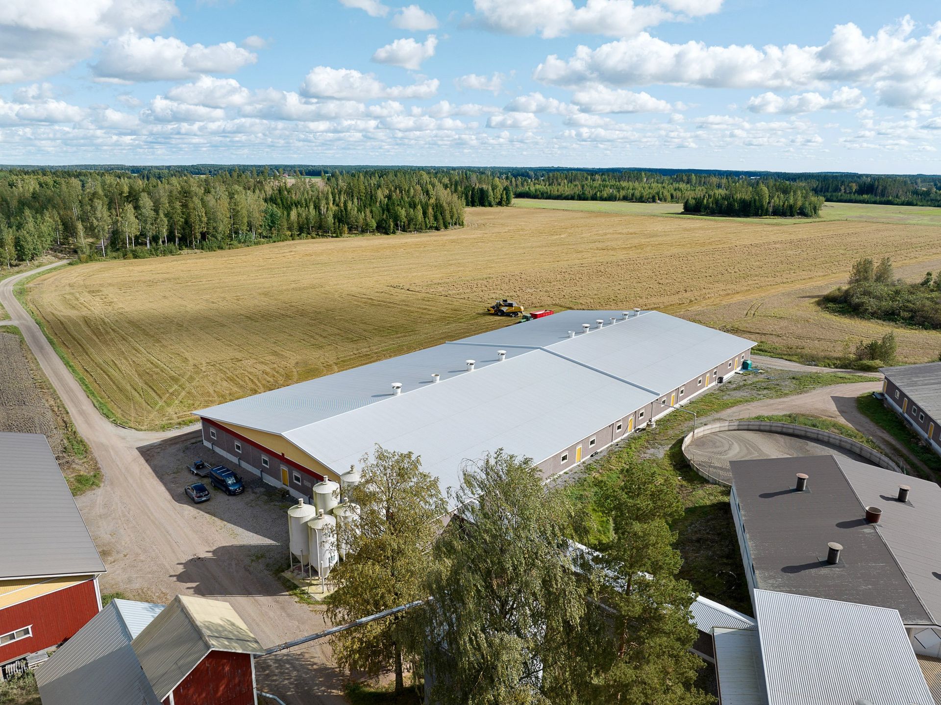 Ilmakuva suuresta valkokattoisesta rakennuksesta peltojen ja puiden vieressä pilvisen taivaan alla