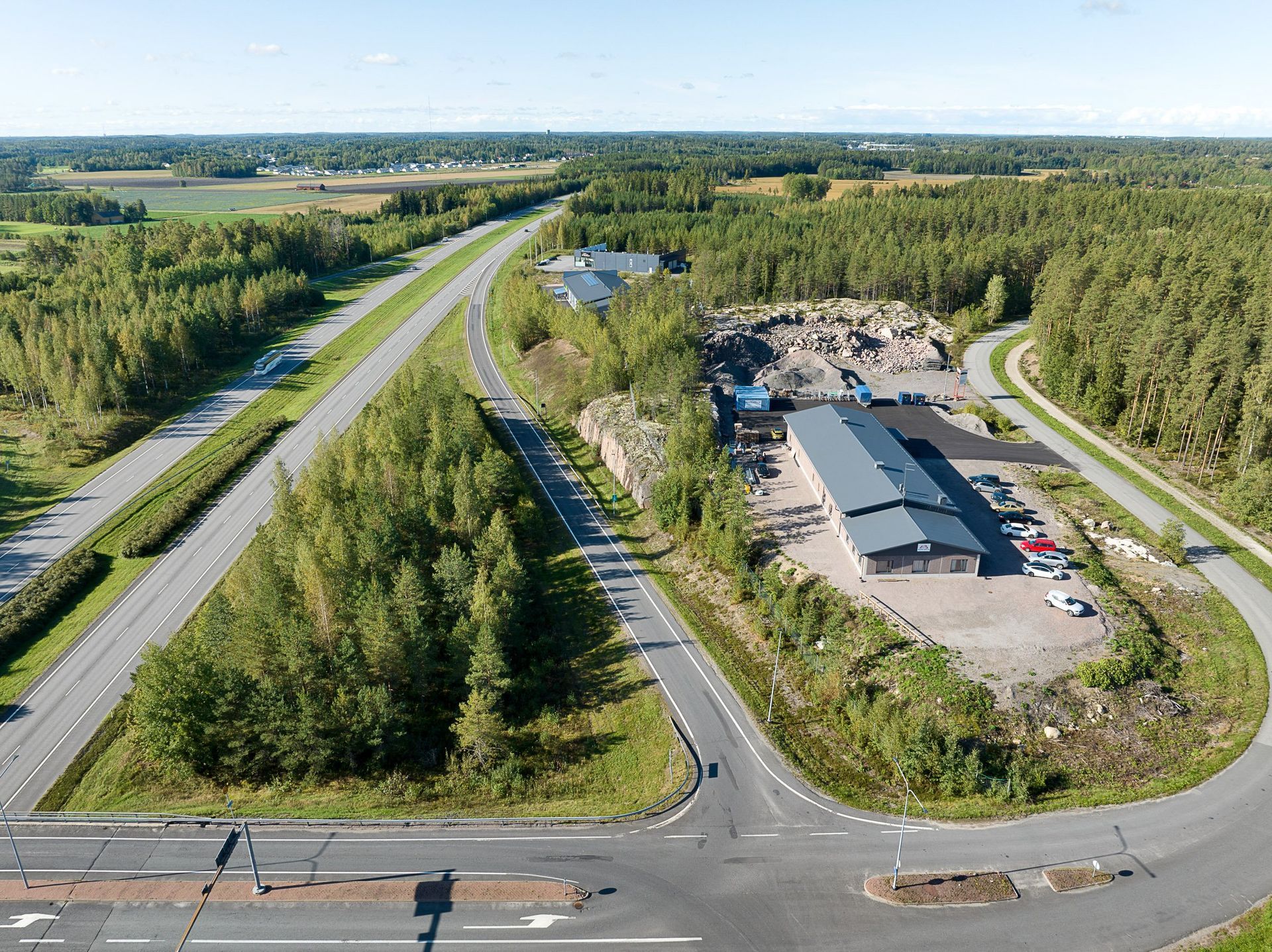 Ilmakuva maaseudun teiden risteyksestä metsäisen teollisuusalueen ja avoimien peltojen vieressä