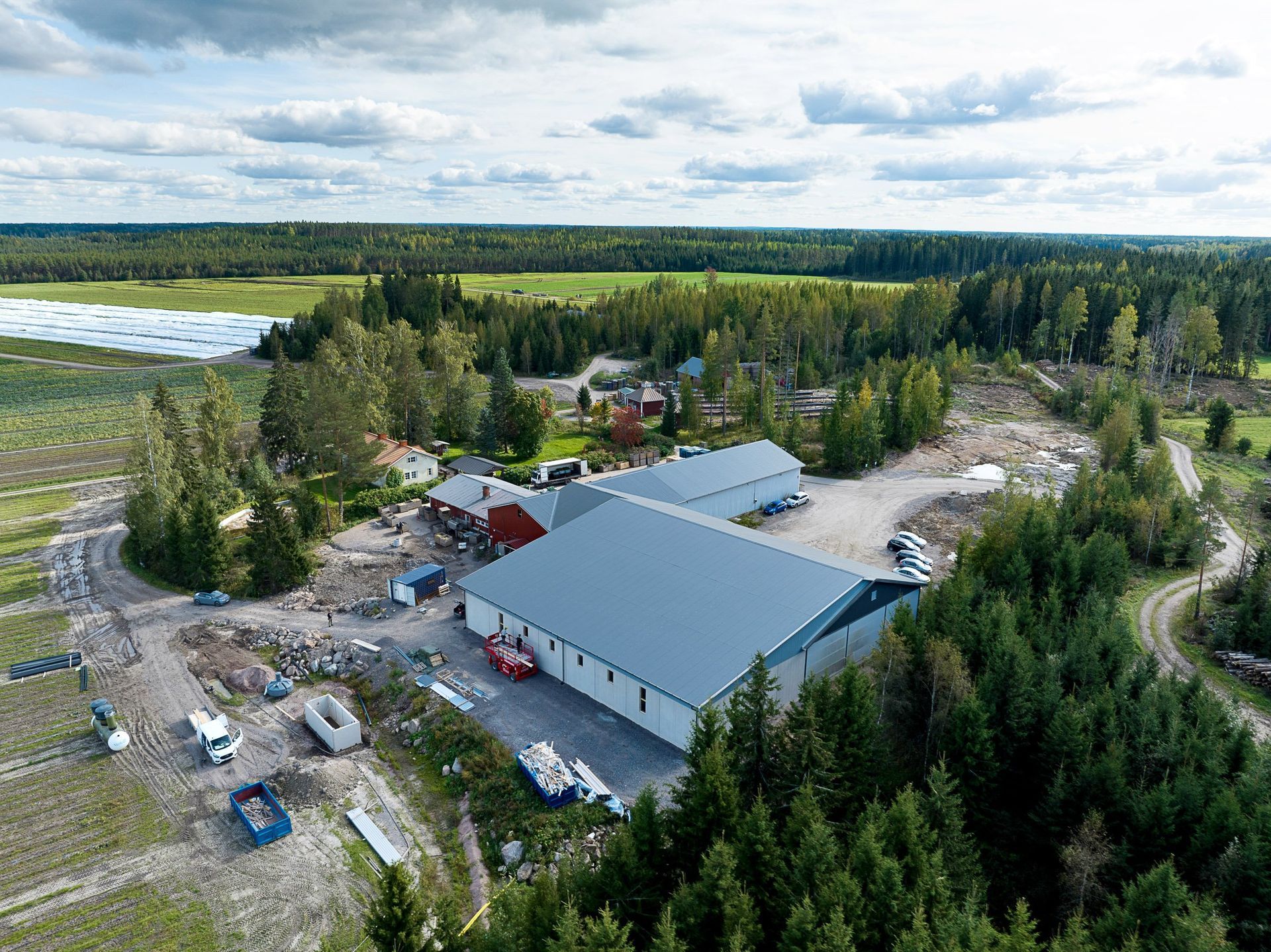 Ilmakuva suuresta harmaakattoisesta rakennuksesta, jota ympäröi metsä ja avoin maa pilvisen taivaan alla