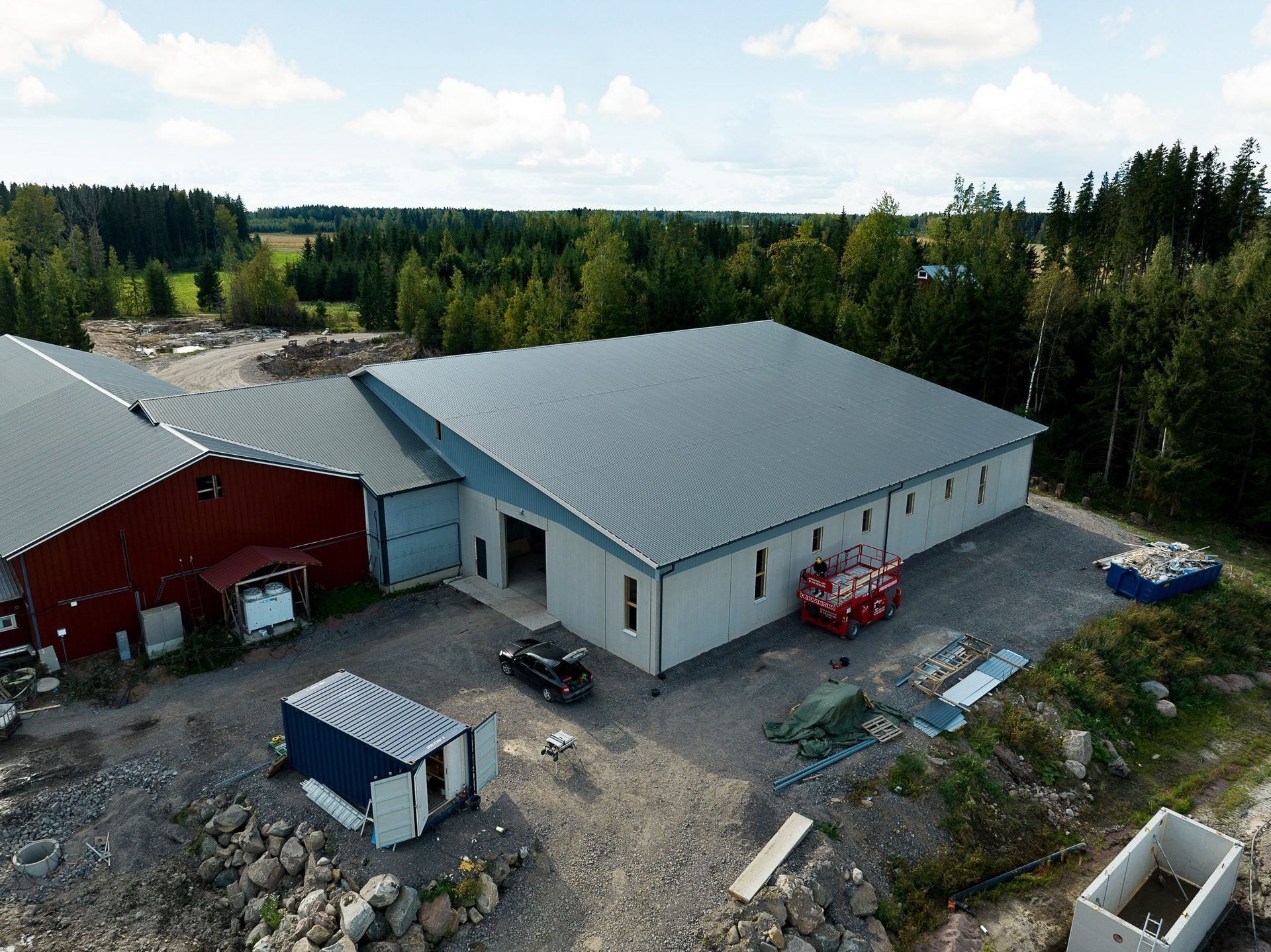 Ilmakuva maaseudun teollisuuspihasta, jossa on suuria harmaakattoisia rakennuksia, kuorma-autoja ja puita.
