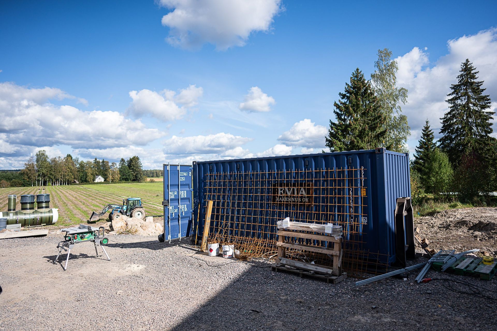 Sininen merikonttityöpaja ulkona soralla työkalujen ja laitteiden kanssa osittain pilvisen taivaan alla