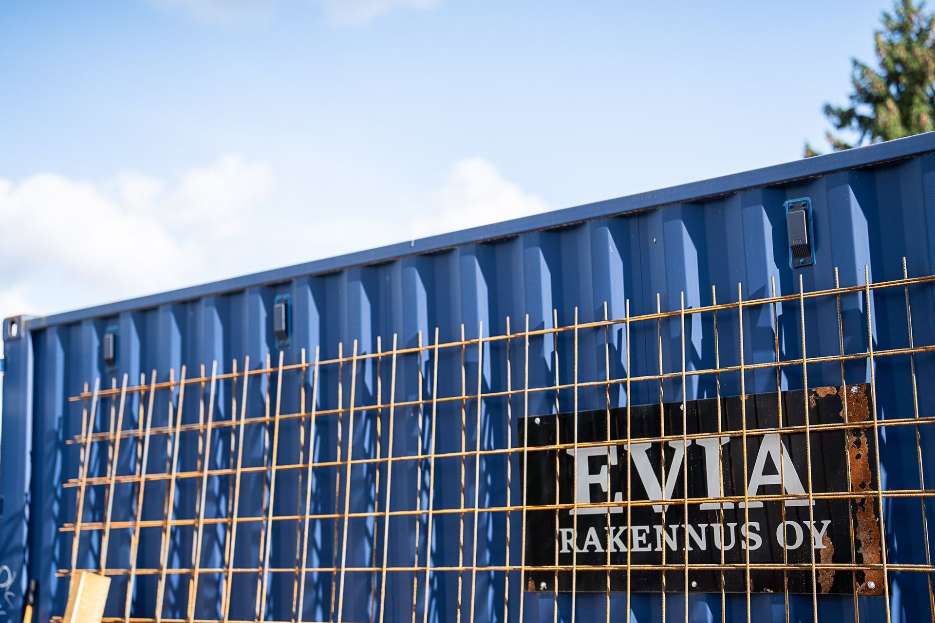 Sininen metallirakennus ruosteisen aidan takana, jossa on EVIA-kyltti kirkkaan taivaan alla