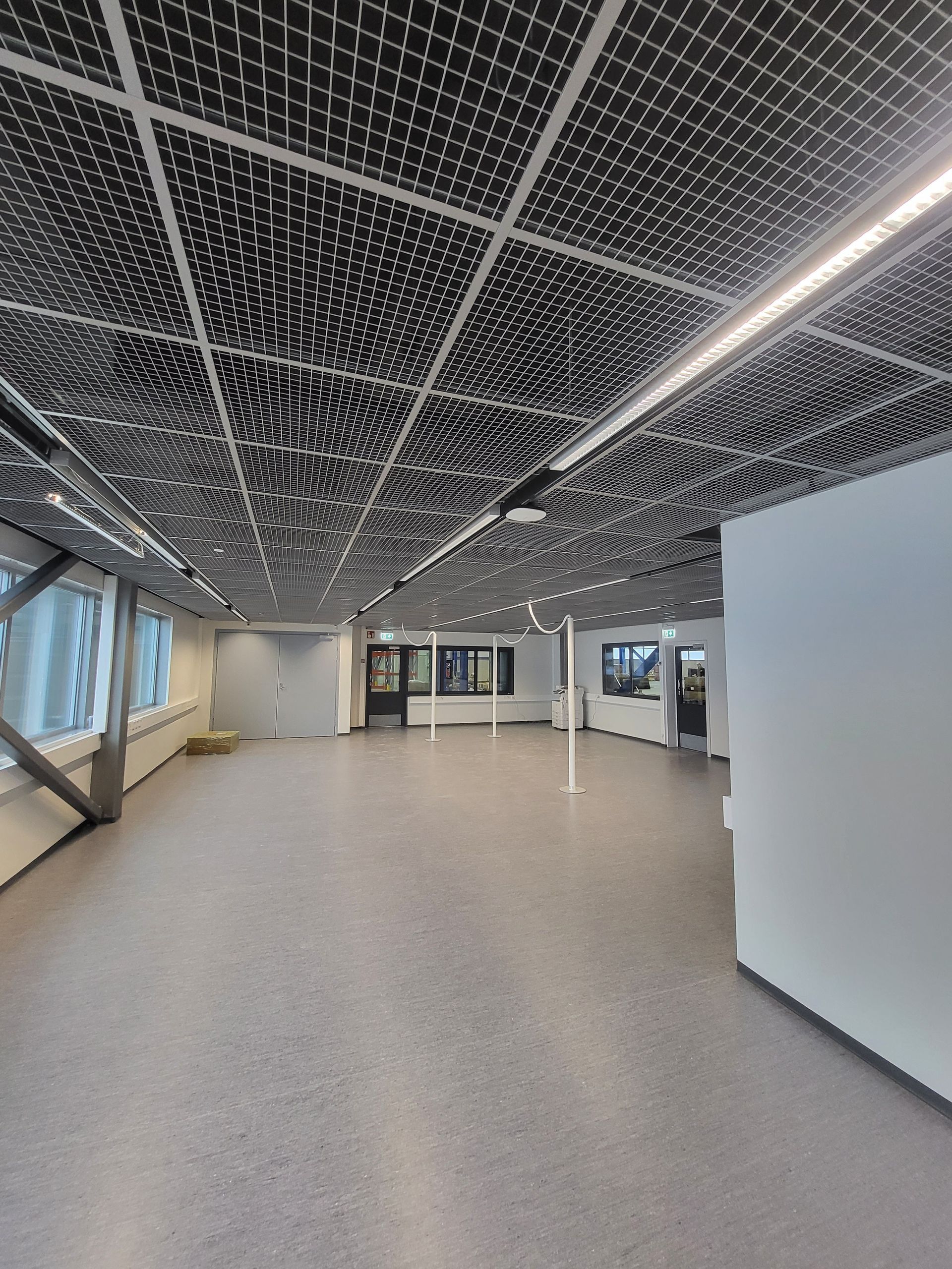 Tyhjä moderni aula, jossa on kuviollinen musta katto, harmaa lattia ja lasiseinät.