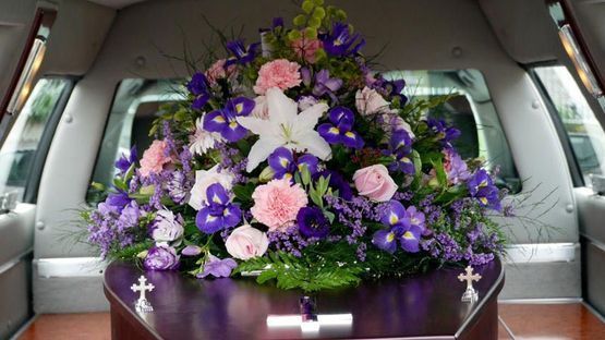 Un ataúd con un ramo de flores de color púrpura y rosa en la parte trasera de un automóvil.