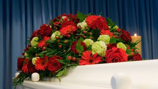 Un ataúd blanco decorado con flores rojas y verdes y una vela.