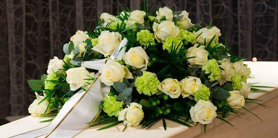 Un ataúd con un ramo de rosas blancas y claveles verdes encima.