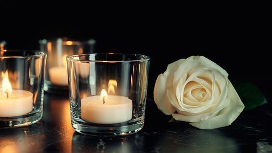 Una rosa blanca está sentada junto a velas en vasos sobre una mesa.