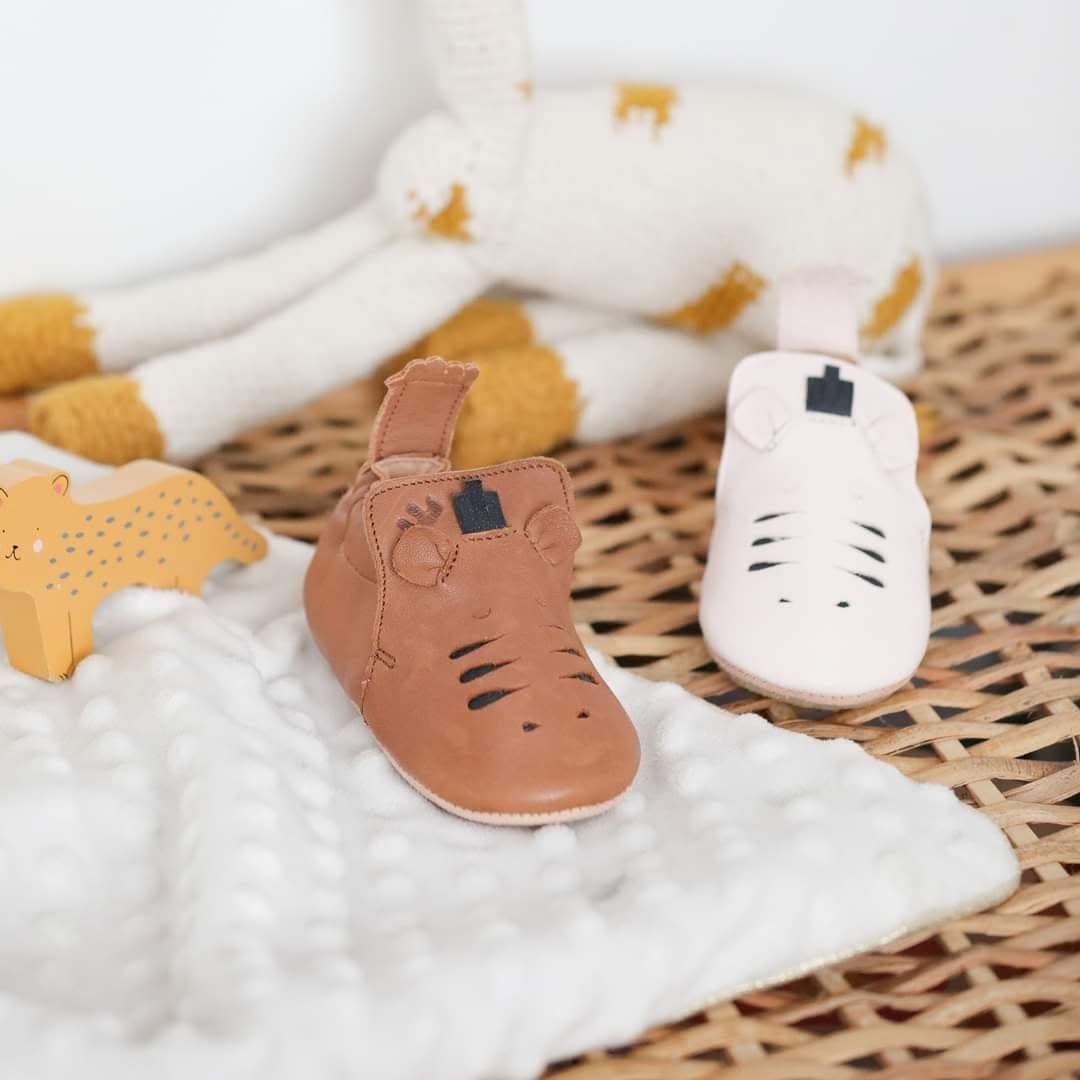 De minuscules chaussures de bébé blanches, beiges et marron sur un tapis tissé avec un fond de couverture douce