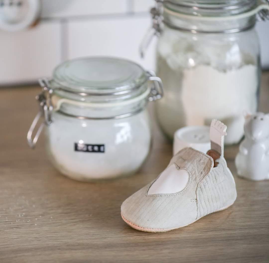 Chaussure blanche de bébé sur une table en bois avec deux bocaux en verre en arrière-plan