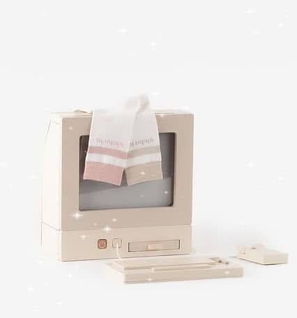 Ordinateur beige minimaliste avec des chaussettes pastel douces posées sur l'écran, sur fond blanc.