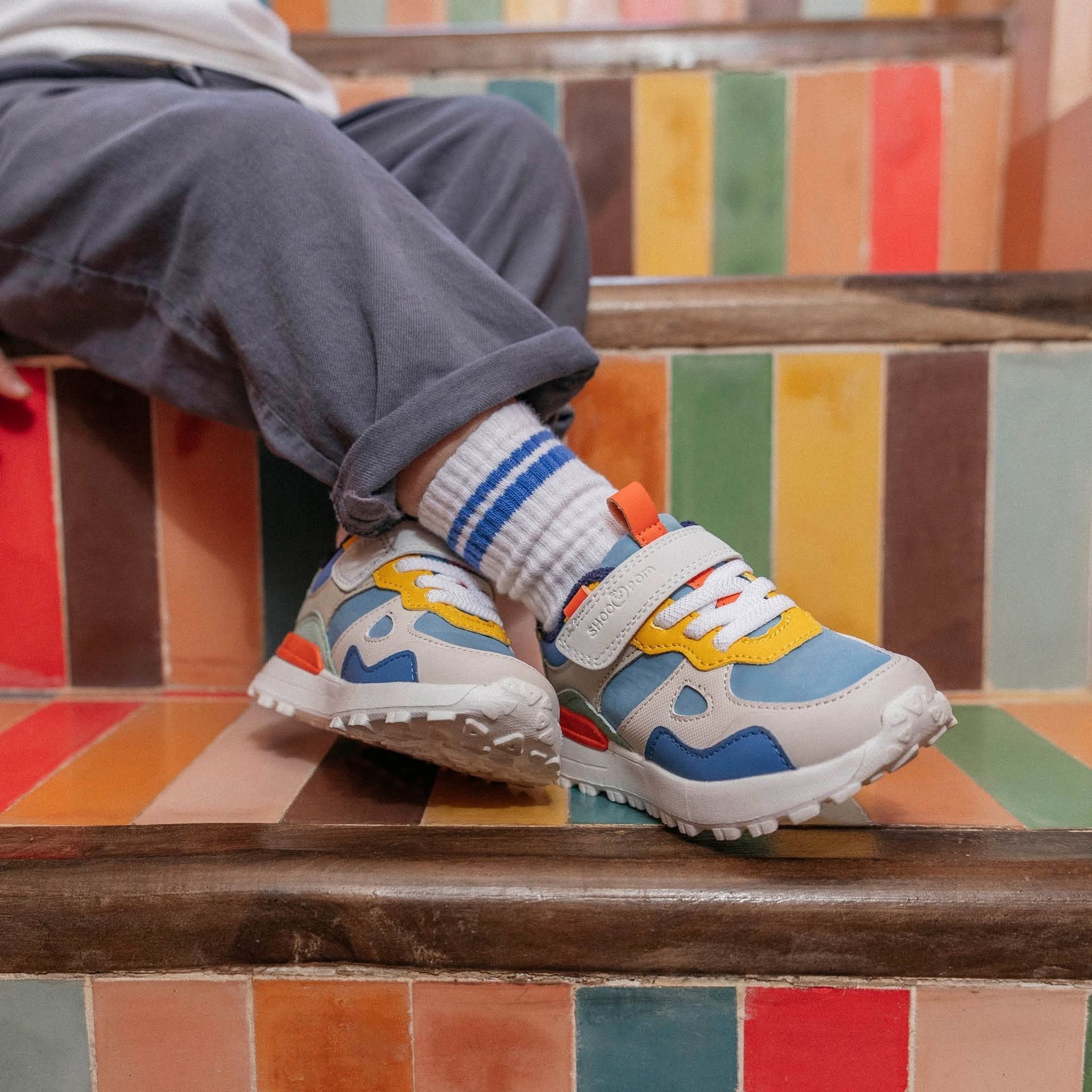 Baskets colorées et chaussettes rayées, jambes croisées, assise sur des marches carrelées multicolores