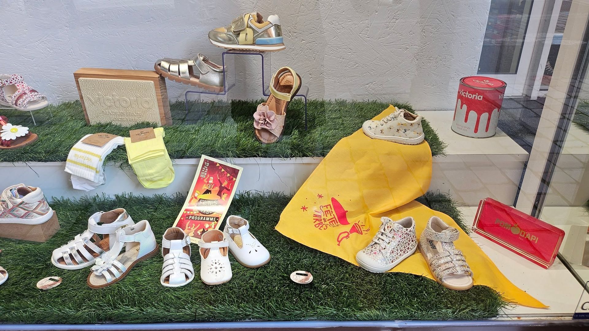 Scène miniature extérieure avec de minuscules chaussures, une forme en tissu jaune et de petits objets disposés sur un gazon synthétique.