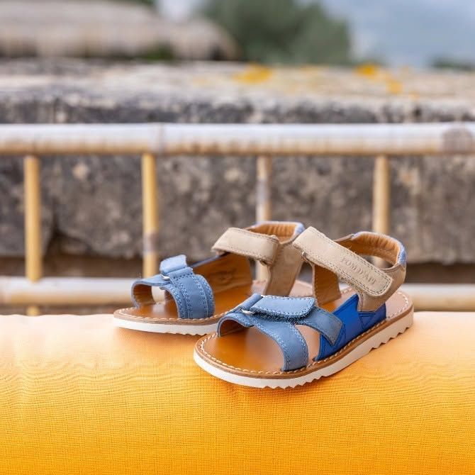 Sandales bleues et beiges pour tout-petits sur un coussin orange à l'extérieur