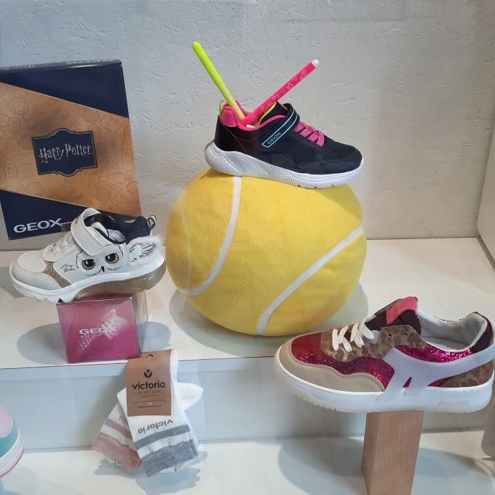 Trois paires de baskets présentées sur de petits supports autour d'une grosse balle de tennis jaune et de boîtes à chaussures