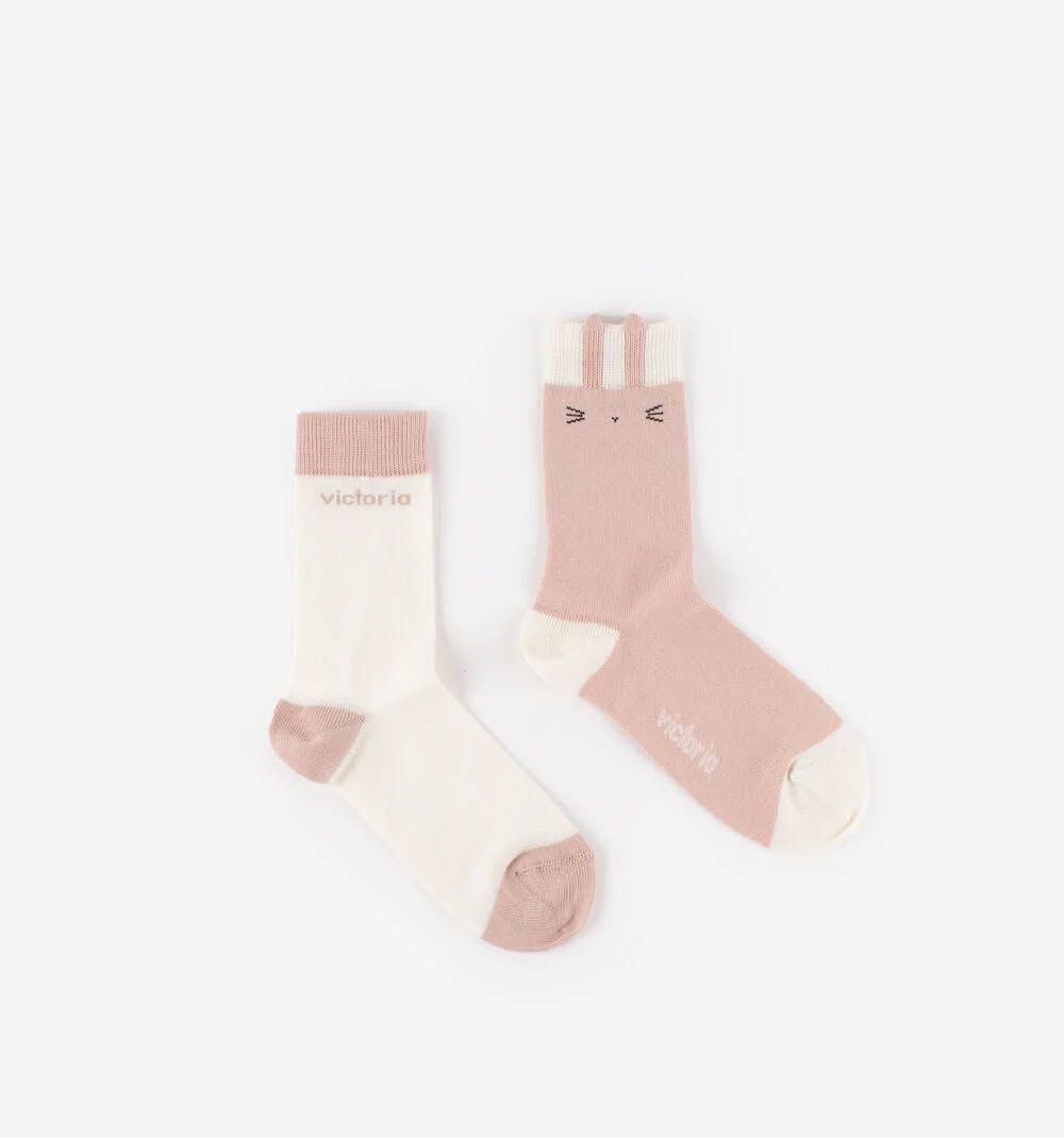 Deux chaussettes pastel, l'une crème et l'autre rose, posées sur un fond blanc.