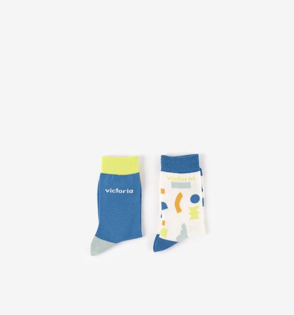 Deux chaussettes à motifs, l'une bleue à revers jaune et l'autre blanche à motifs colorés, sur fond blanc.
