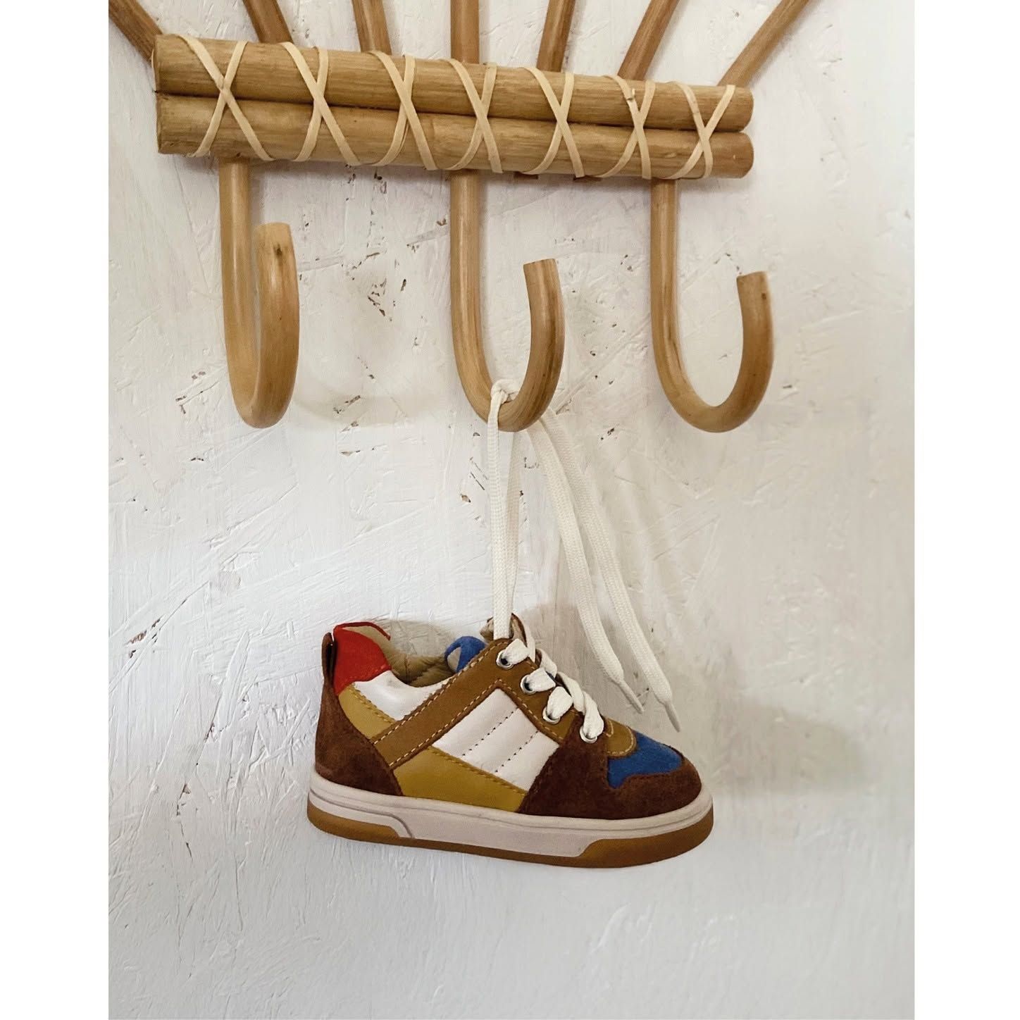 Porte-manteau mural en bois avec trois crochets au-dessus d'une basket multicolore accrochée sur un mur blanc