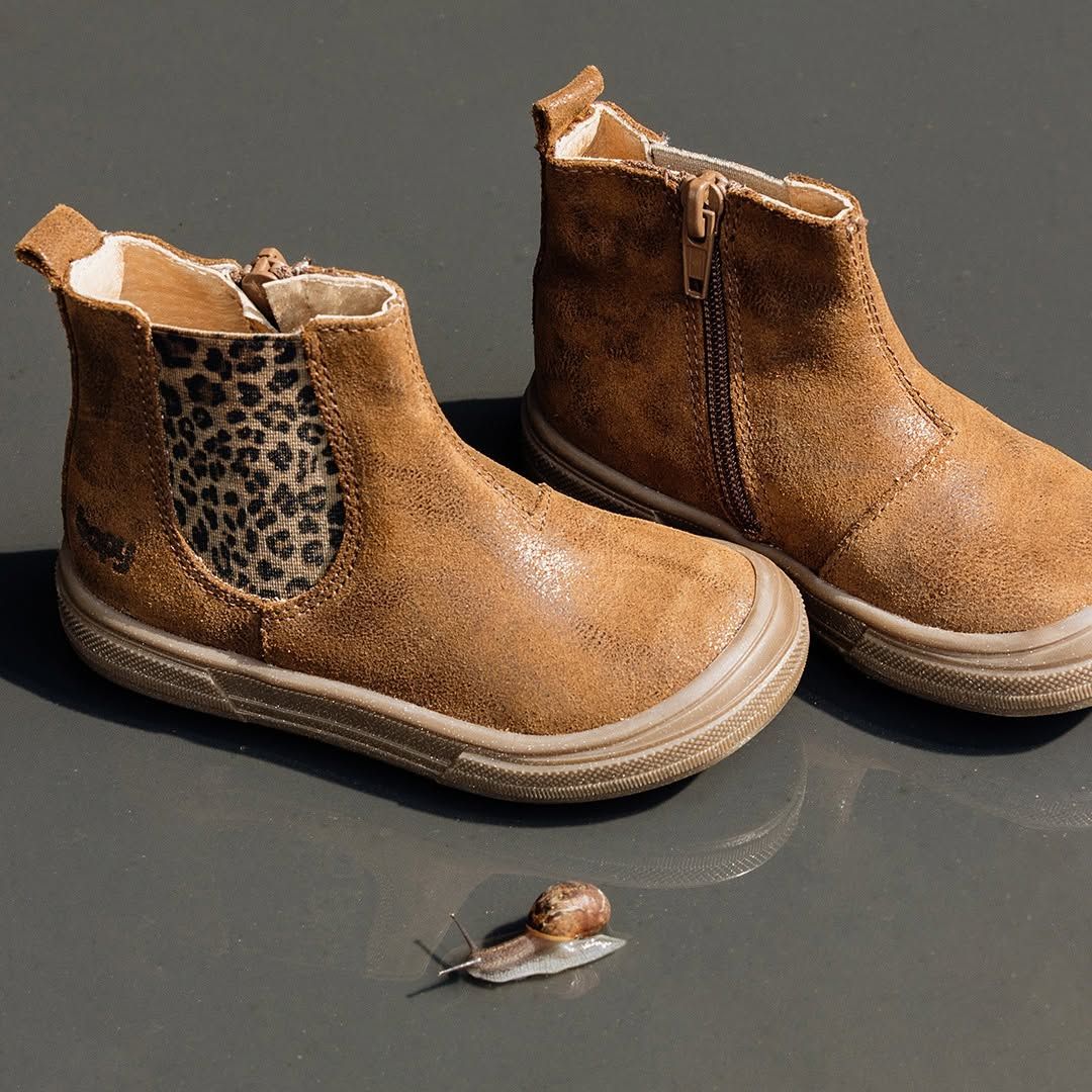 Deux petites bottes marron pour enfant sur une surface sombre, avec un petit escargot devant elles.