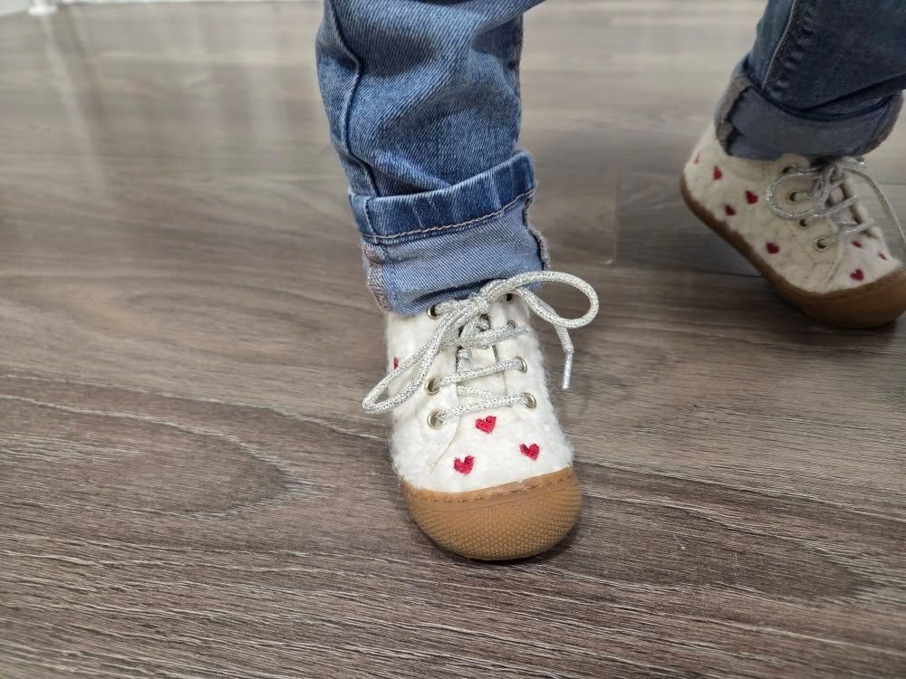 Gros plan sur une basket blanche à cœurs rouges d'enfant marchant sur un parquet.