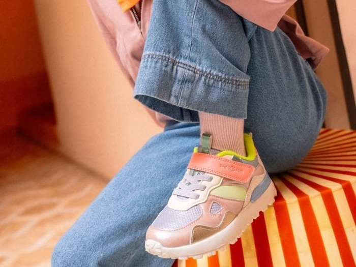 Le pied d'un enfant chaussé d'une basket pastel repose sur un escalier à rayures orange et blanches.