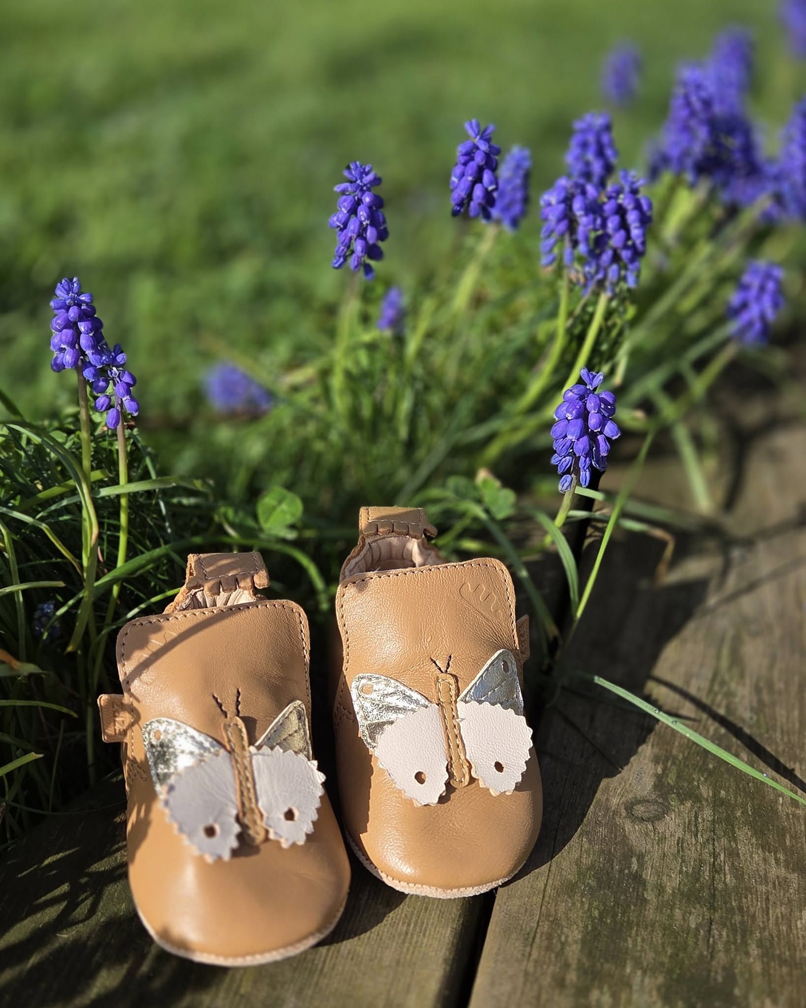 Chaussures de bébé beiges à motifs de papillons blancs parmi des fleurs violettes sur des marches en pierre