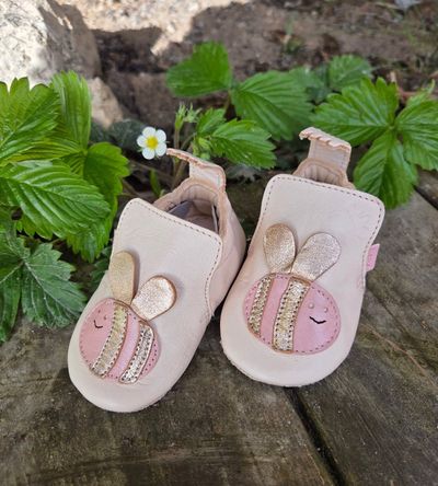 Chaussons roses en forme de lapin sur un rocher, avec des feuilles vertes et une petite fleur blanche derrière.