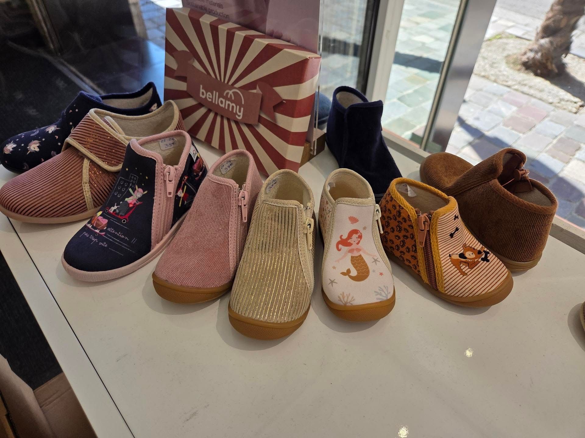 Des chaussures d'enfants colorées alignées sur une table d'exposition près d'une vitrine