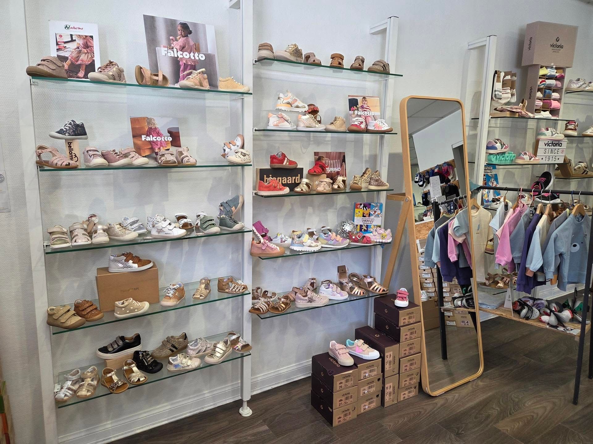 Vitrine de boutique avec étagères à chaussures, objets de décoration et portant à vêtements à côté d'un miroir en pied